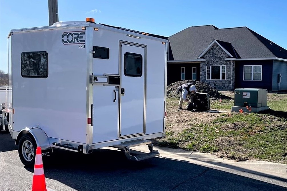 Exterior action shot of a fiber splicer working in front of a newer built home, an orange cone is out in front for safety